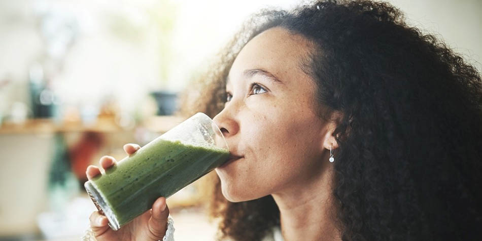 A woman sips a green smoothie.