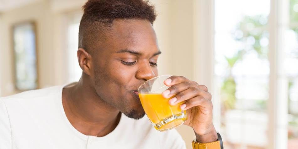 A man drinks a glass of orange juice.
